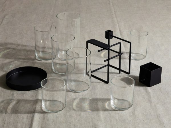 Minimalist Bauhaus style cylindrical glassware and geometric black metal candleholder on raw linen